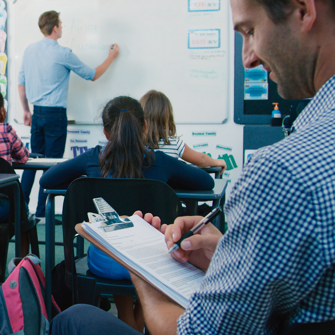 Teacher writing on whiteboard in classroom whilst being observed